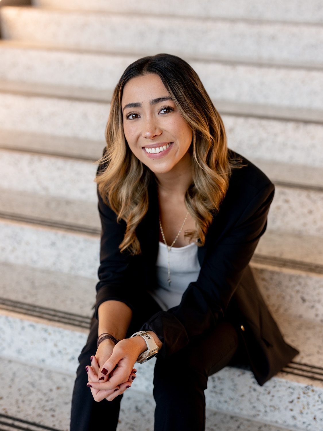 María sitting on a staircase, leaning forward with her hands clasped, smiling