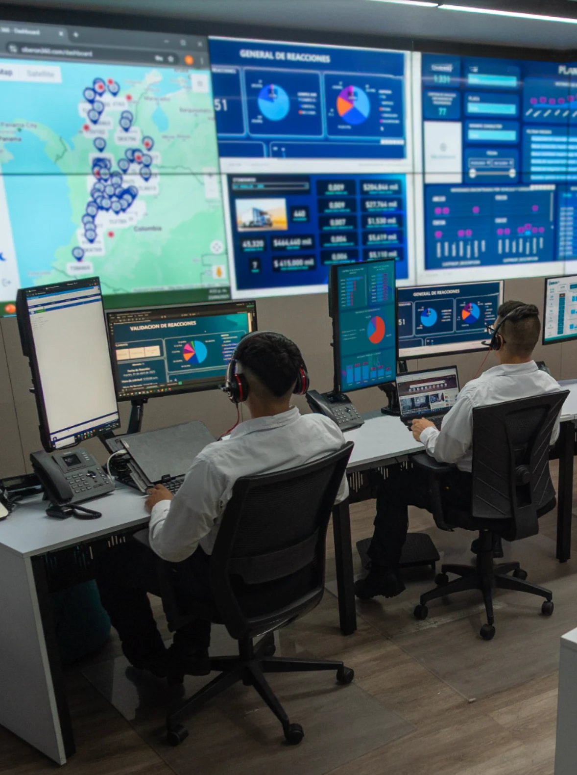 Oberon's monitoring center: two operators with headsets at their workstations, facing a video wall of maps and live dashboards