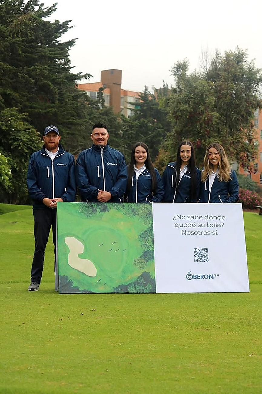 María with the Oberon TSI team on the golf course, next to the banner that reads ¿No sabe dónde quedó su bola? Nosotros sí.